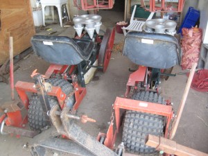 The new transplanter, a two-row Mechanical 4000, parked in our pole building for now. Note the SEATS. Cushy. The starts get dropped in the little rotating cones and then tamped in as the transplanting rolls along.