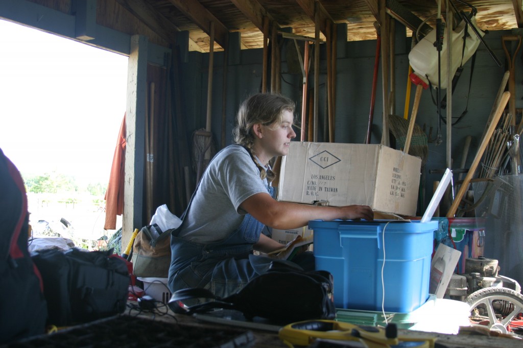 A photo from the farm archive: me (Katie) writing in our first farm "office" -- a shed on the land we rented in 2006. I composed many an early blog post with that laptop propped on bins of seeds!